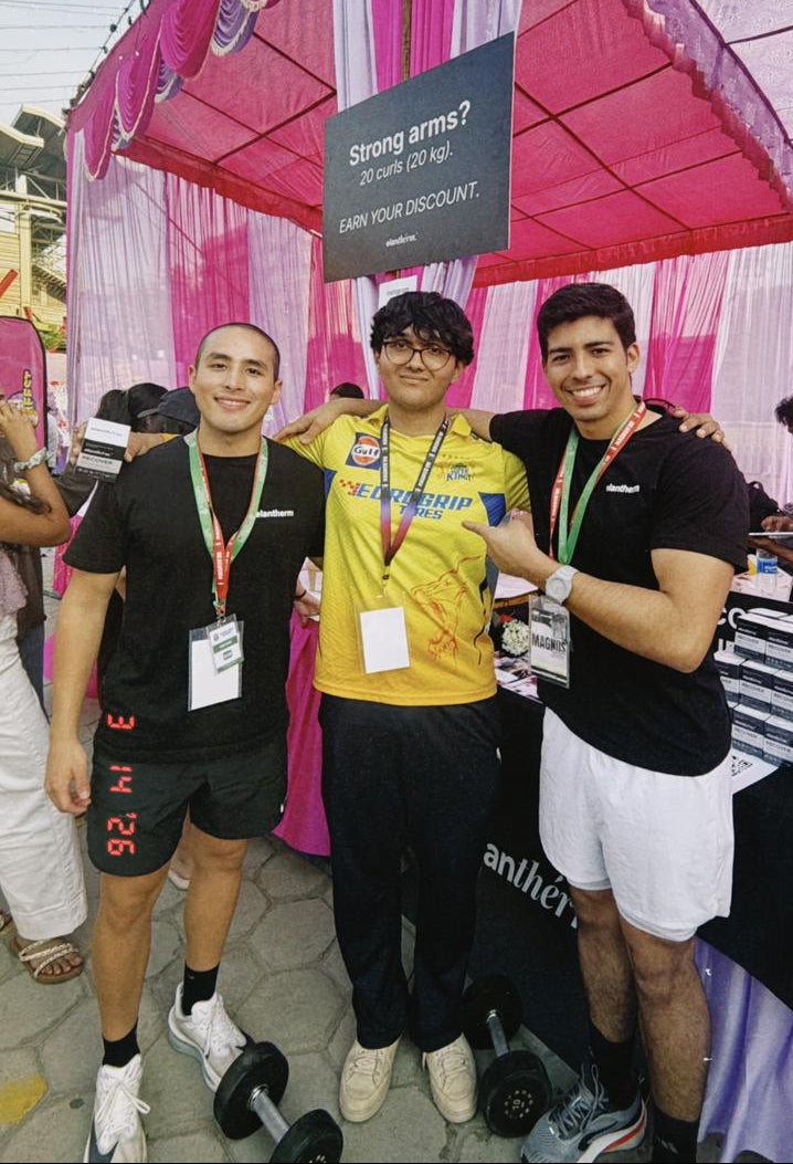 Three men posing together in front of a pink and white tent with promotional materials.